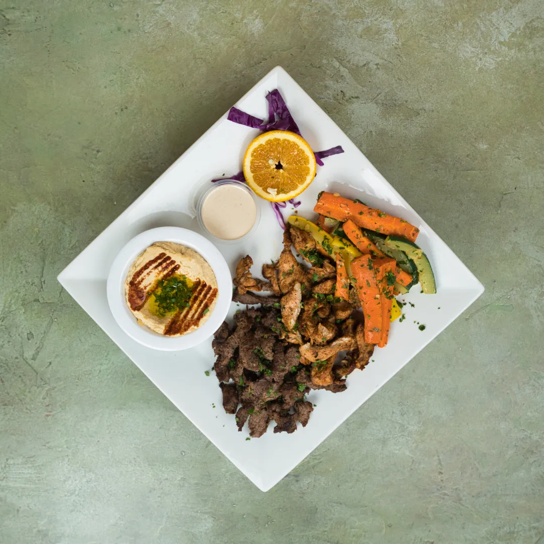 Half beef, half chicken shawarma plate with hummus, sautéed vegetables, and a cup of sauce