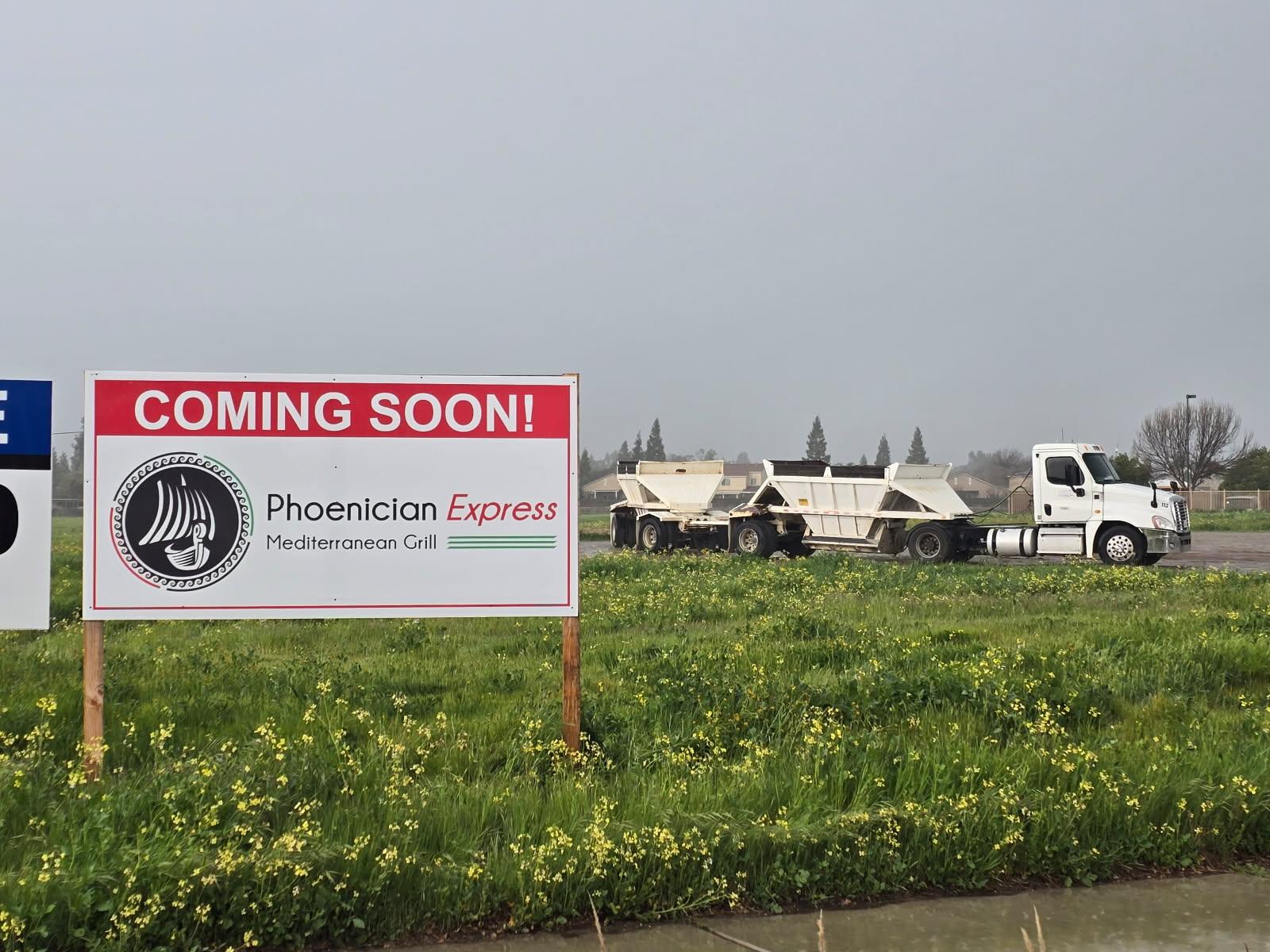 Coming Soon sign at the future Phoenician Express location in Clovis, with construction equipment behind it